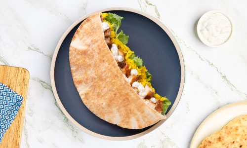 a stuffed pita on a blue plate with a side of tzatziki sauce